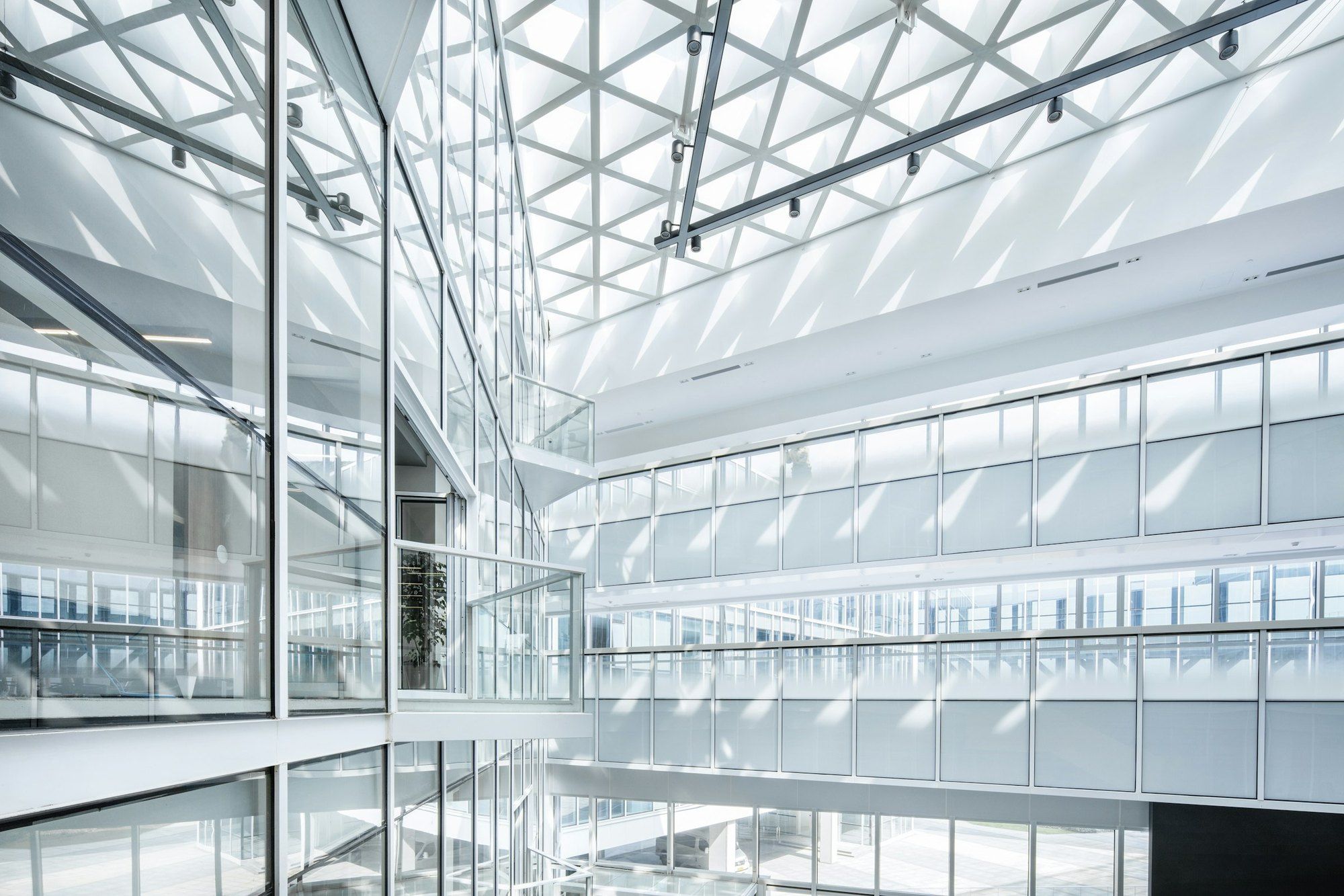 White interior atrium of an office building, with a triangular lattice roof and glass walls