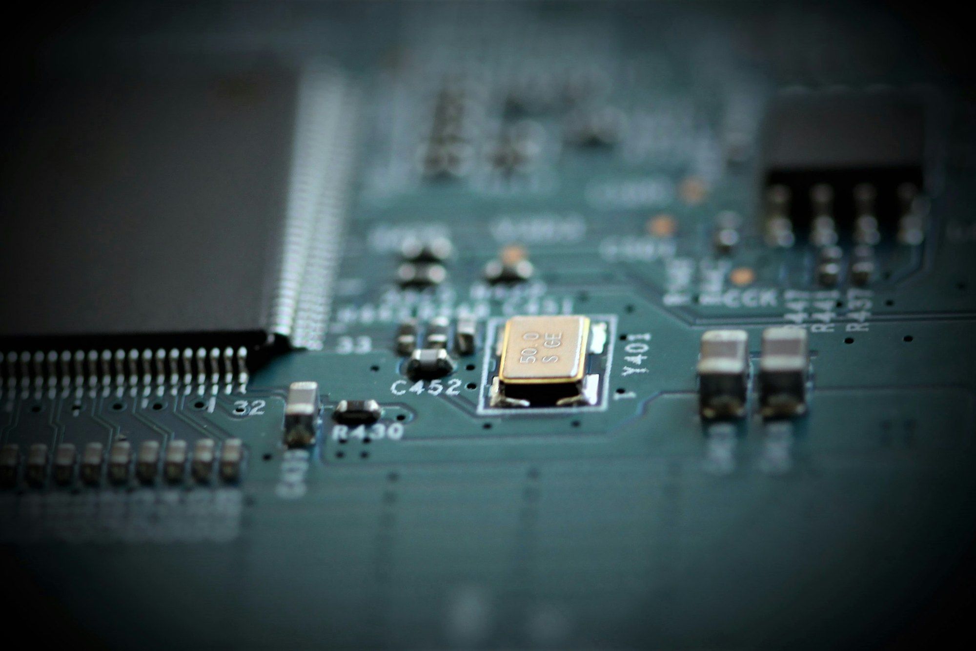 Close-up of components soldered on a circuit board, with a gold quartz crystal in focus