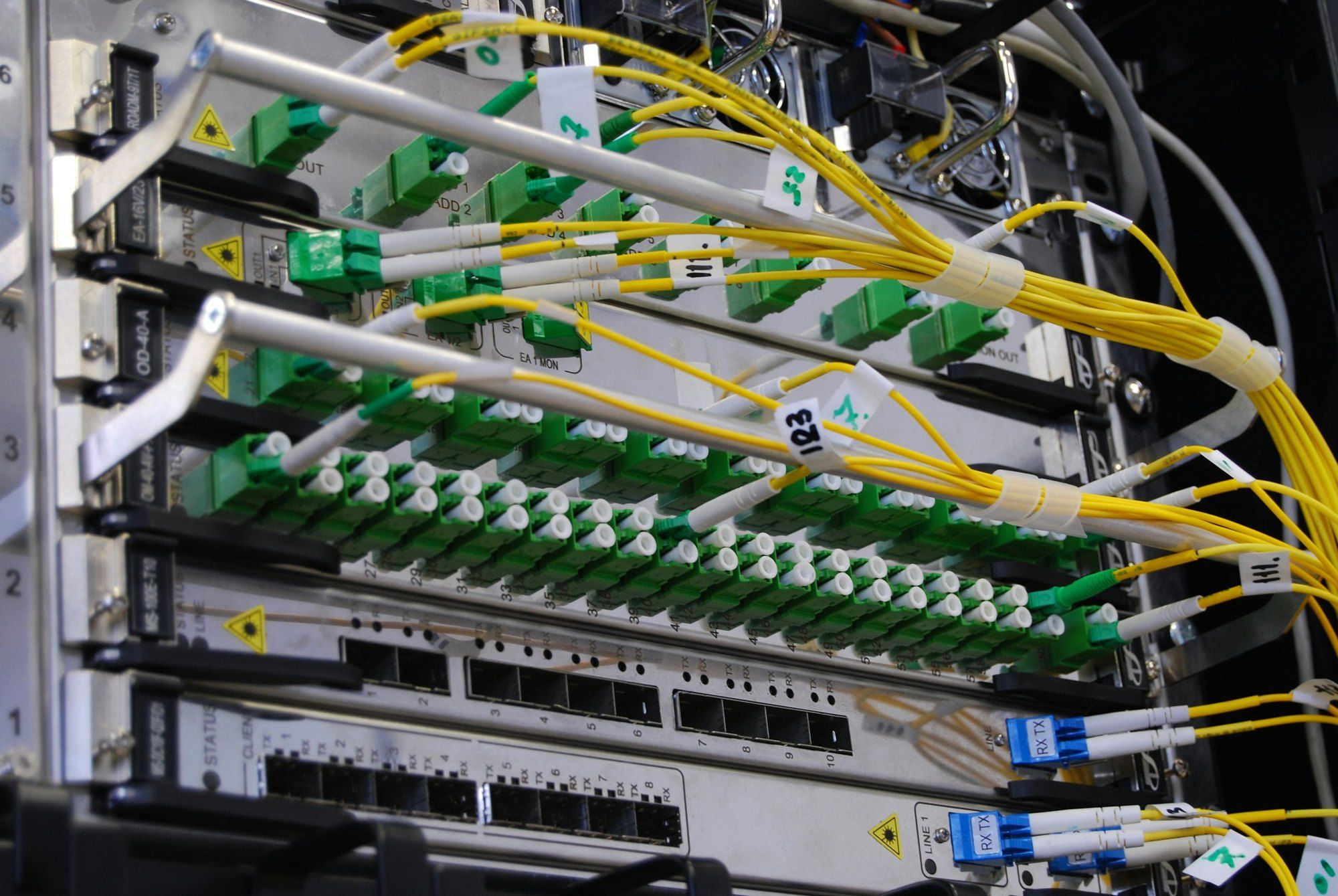 Communications equipment in a rack, with green fibre connectors and grouped yellow cables