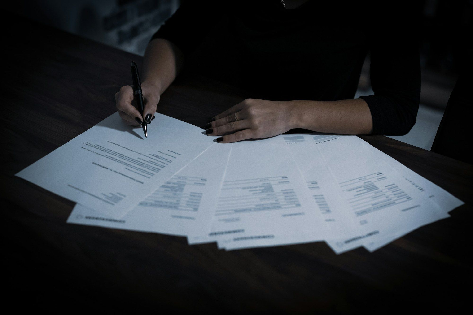 Hands going over several printed sheets fanned out on a dark table, pen in hand